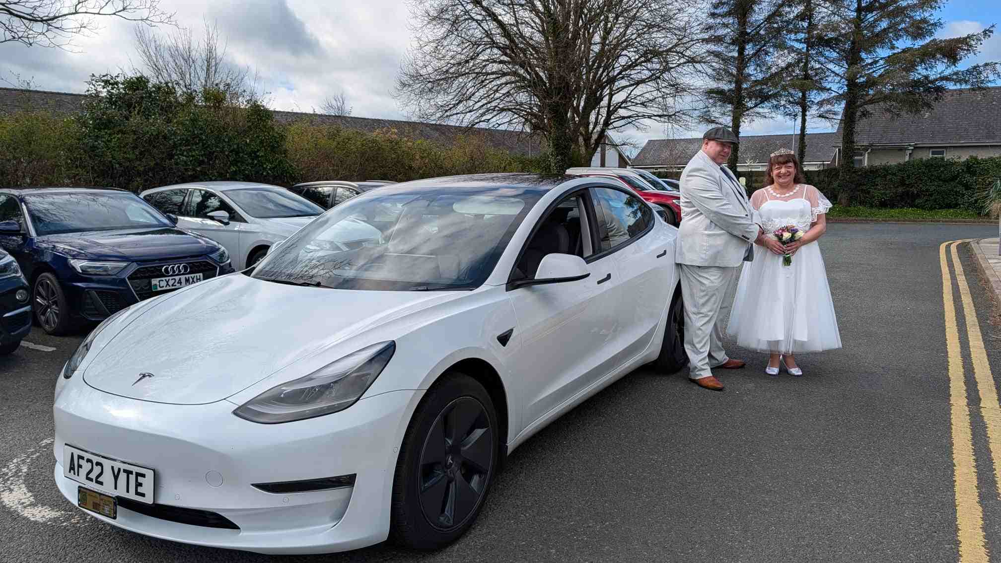 Wedding transfer in Pwllheli, North Wales, with a white Tesla Model 3 and a newlywed couple on their special day.